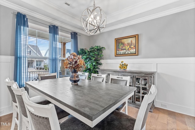 dining area featuring visible vents, ornamental molding, wood finished floors, an inviting chandelier, and wainscoting