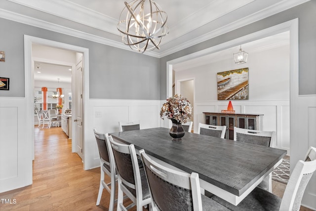 dining area featuring light wood finished floors, a notable chandelier, wainscoting, and crown molding