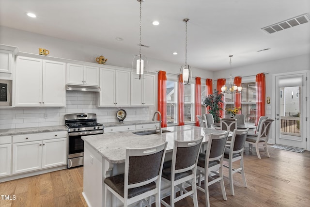 kitchen featuring visible vents, under cabinet range hood, light wood-style flooring, stainless steel appliances, and a sink