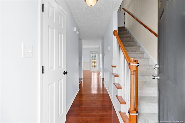 hallway with a textured ceiling, stairway, dark wood finished floors, and baseboards