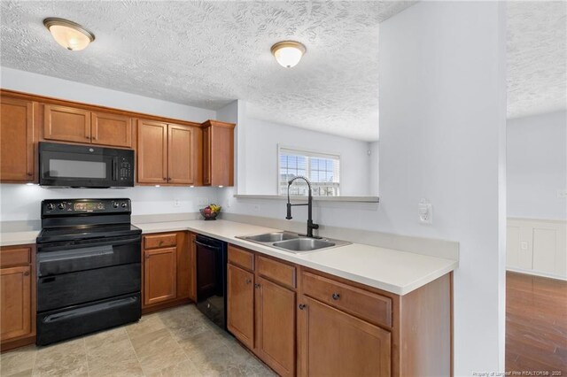 kitchen with brown cabinetry, light countertops, a sink, and black appliances