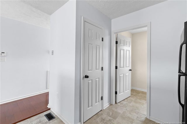 hall with visible vents, a textured ceiling, and baseboards