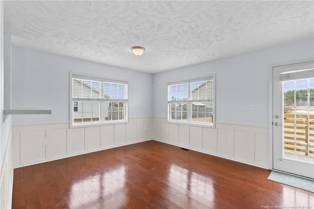 spare room with wood-type flooring, a wealth of natural light, and wainscoting