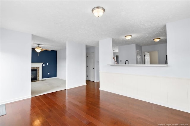 unfurnished living room featuring a glass covered fireplace, ceiling fan, a textured ceiling, wood finished floors, and baseboards