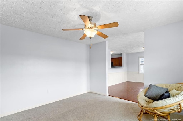 unfurnished room featuring a ceiling fan, carpet, a wainscoted wall, and a textured ceiling