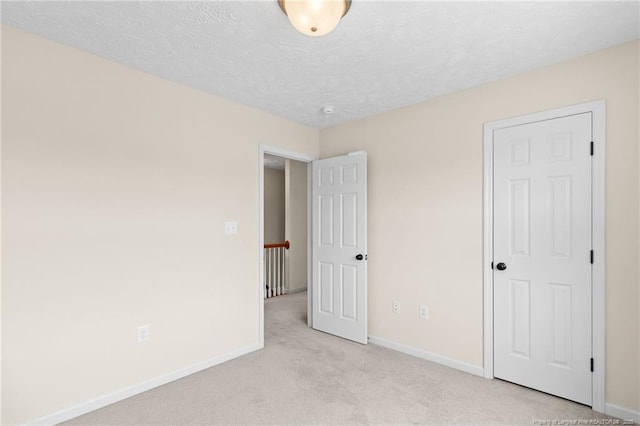 unfurnished bedroom featuring light carpet, a textured ceiling, and baseboards