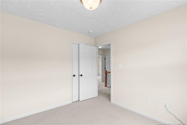 unfurnished bedroom featuring light carpet, a closet, a textured ceiling, and baseboards