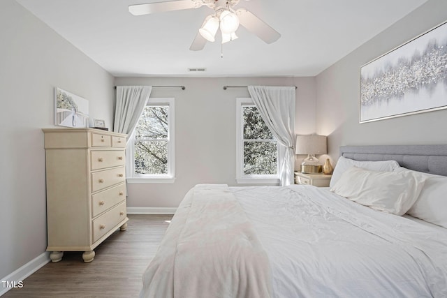 bedroom with a ceiling fan, wood finished floors, visible vents, and baseboards