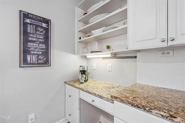 kitchen with built in study area, open shelves, stone countertops, white cabinets, and backsplash