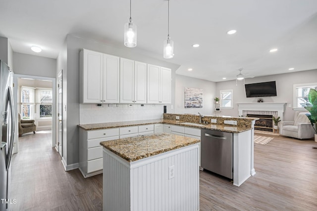 kitchen with a sink, wood finished floors, open floor plan, stainless steel appliances, and a brick fireplace