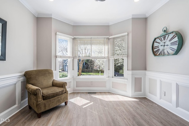 living area featuring visible vents, crown molding, a wainscoted wall, wood finished floors, and a decorative wall