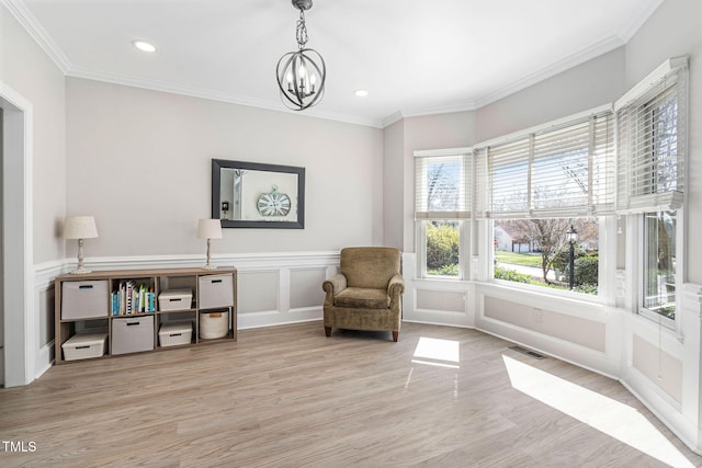 living area with visible vents, light wood finished floors, ornamental molding, a decorative wall, and a chandelier