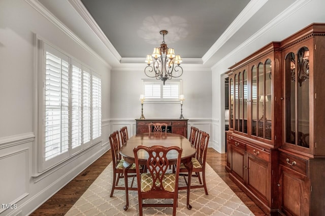 dining space with a tray ceiling, a wainscoted wall, a notable chandelier, and wood finished floors