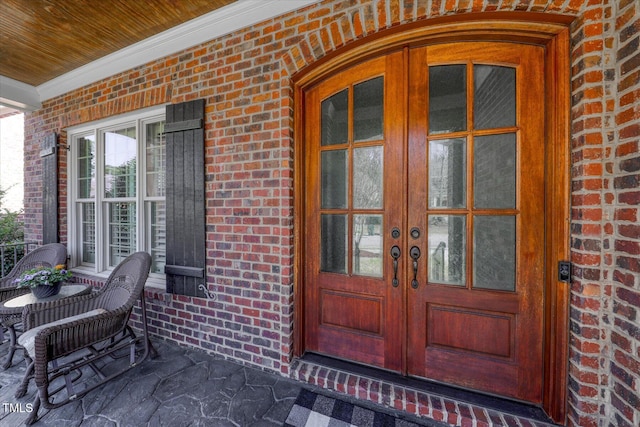 entrance to property with french doors, brick siding, and covered porch