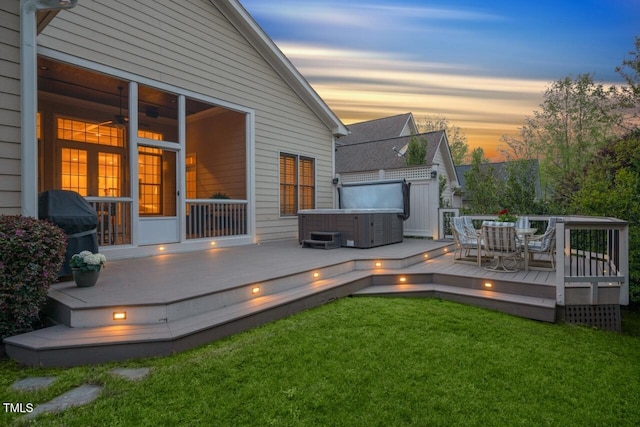 deck at dusk with a lawn and a hot tub