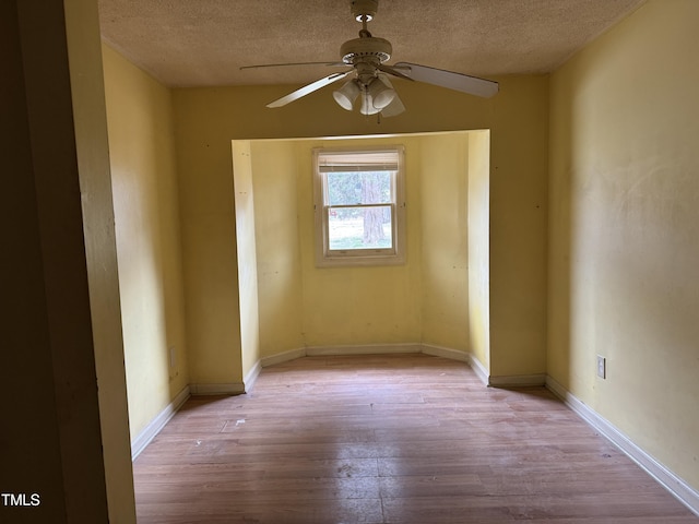 unfurnished room with wood-type flooring, a ceiling fan, a textured ceiling, and baseboards