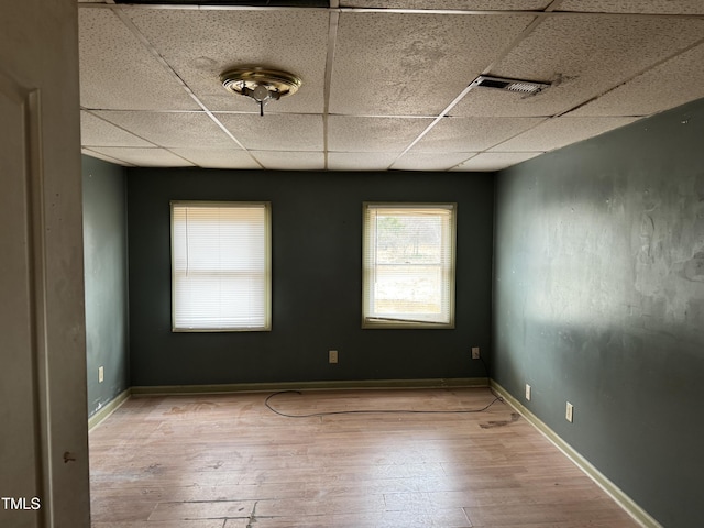 empty room with baseboards, wood-type flooring, a drop ceiling, and visible vents