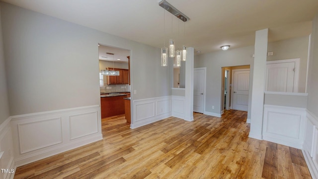 unfurnished dining area featuring a wainscoted wall, light wood-style flooring, and a decorative wall