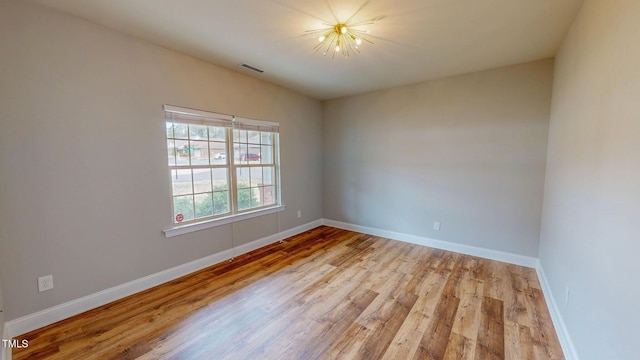 empty room with a chandelier, visible vents, baseboards, and wood finished floors