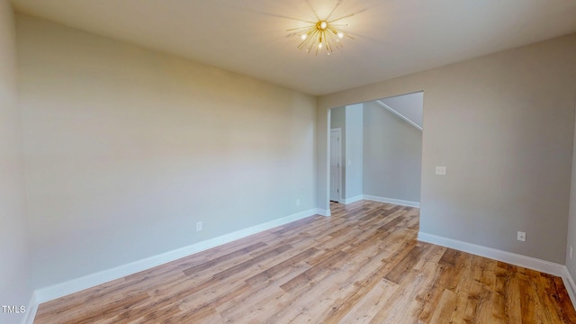 empty room with light wood-style flooring, an inviting chandelier, and baseboards