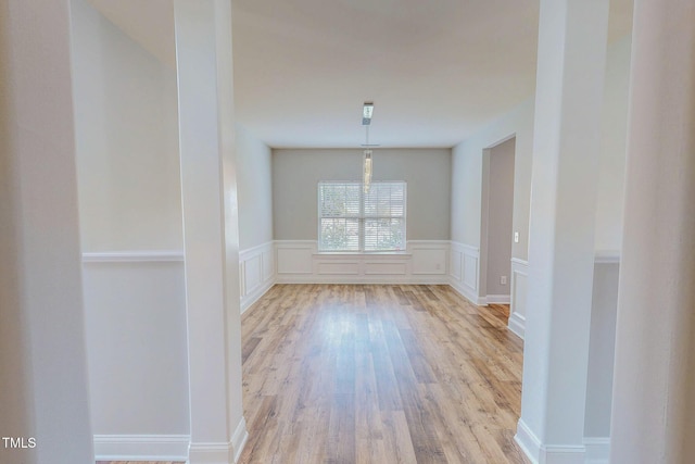 unfurnished dining area with a wainscoted wall, a decorative wall, and light wood-type flooring