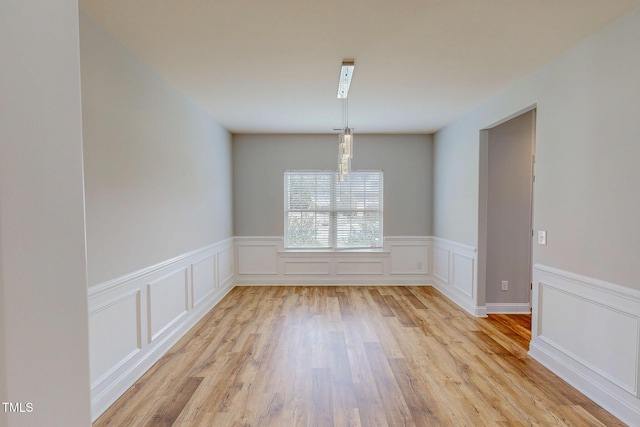 unfurnished dining area with light wood-type flooring and a wainscoted wall