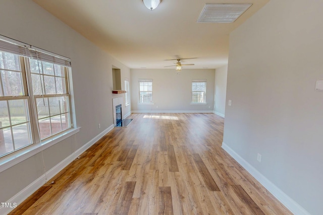 unfurnished living room featuring light wood finished floors, visible vents, baseboards, and a glass covered fireplace