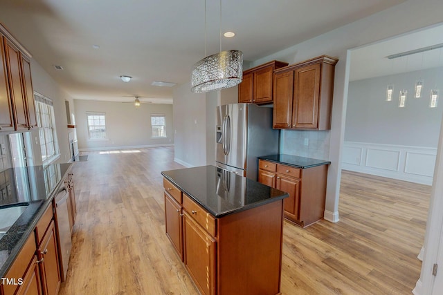 kitchen featuring open floor plan, light wood-type flooring, dark stone countertops, appliances with stainless steel finishes, and brown cabinetry