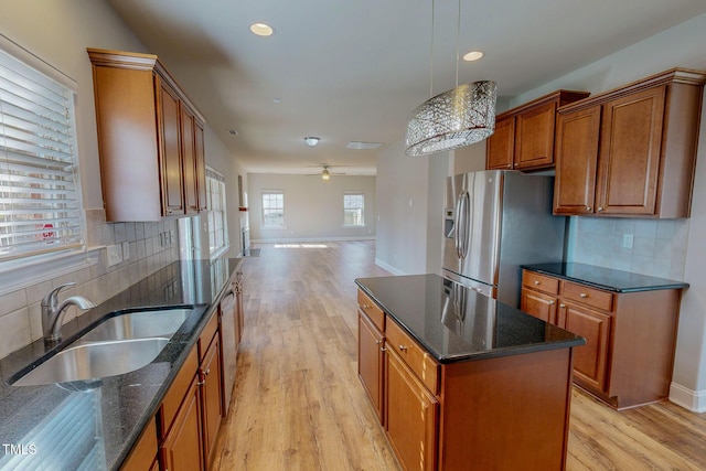 kitchen with dark stone countertops, brown cabinets, a sink, appliances with stainless steel finishes, and light wood-type flooring