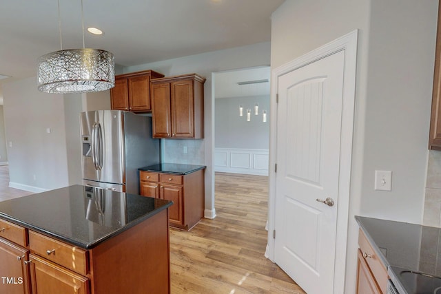 kitchen featuring brown cabinets, stainless steel refrigerator with ice dispenser, decorative light fixtures, dark stone counters, and light wood-style floors