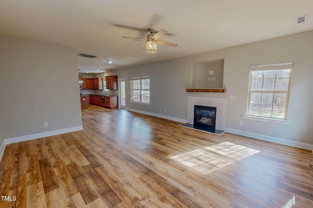 unfurnished living room with visible vents, wood finished floors, baseboards, and a glass covered fireplace