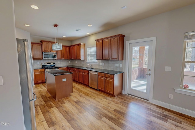 kitchen featuring light wood finished floors, a sink, decorative backsplash, stainless steel appliances, and dark countertops