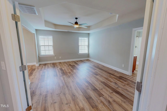 unfurnished room featuring a ceiling fan, wood finished floors, baseboards, visible vents, and a tray ceiling