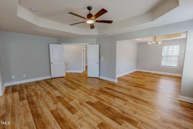 unfurnished room with light wood-style flooring, ceiling fan with notable chandelier, a raised ceiling, and baseboards