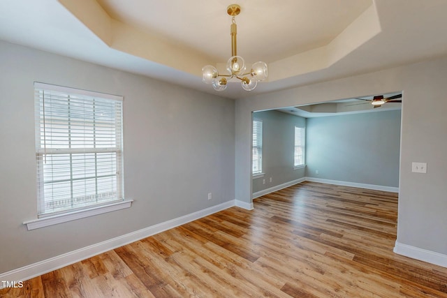 unfurnished room featuring ceiling fan with notable chandelier, a raised ceiling, wood finished floors, and baseboards