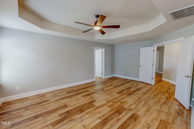 unfurnished bedroom with visible vents, baseboards, a raised ceiling, and light wood-style floors