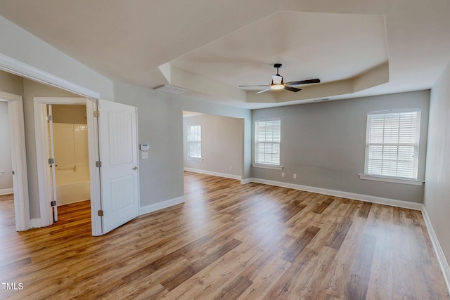 spare room with baseboards, visible vents, light wood-style flooring, ceiling fan, and a raised ceiling