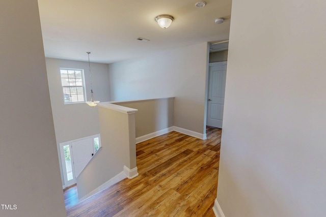 hall with an upstairs landing, visible vents, baseboards, and light wood-style floors