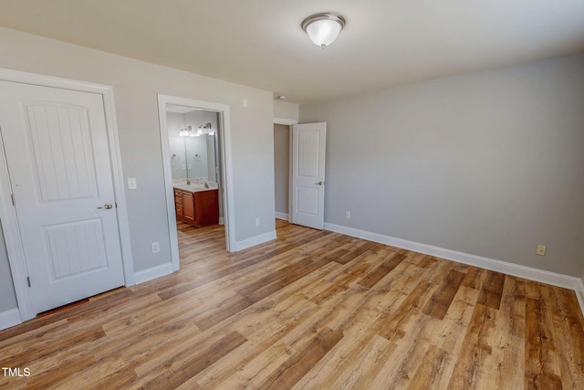 unfurnished bedroom featuring light wood-style flooring, baseboards, and connected bathroom