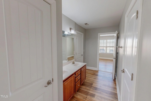 bathroom featuring wood finished floors, visible vents, baseboards, double vanity, and a sink