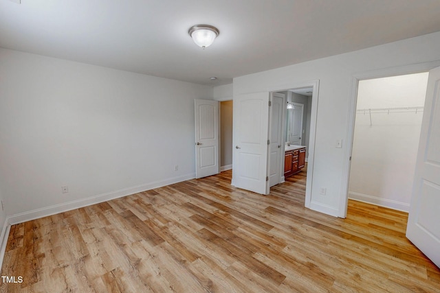 unfurnished bedroom with a walk in closet, baseboards, and light wood finished floors