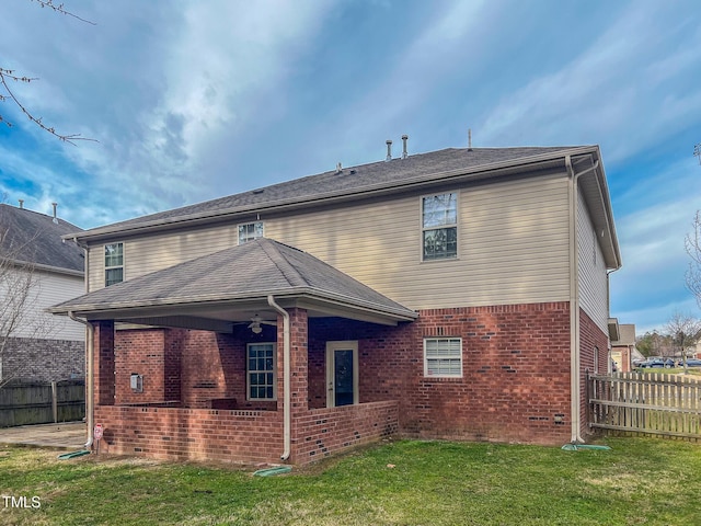 rear view of property featuring brick siding, a shingled roof, ceiling fan, fence, and a yard