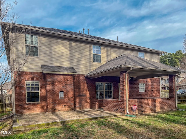 back of house featuring a yard, brick siding, a shingled roof, and a patio area