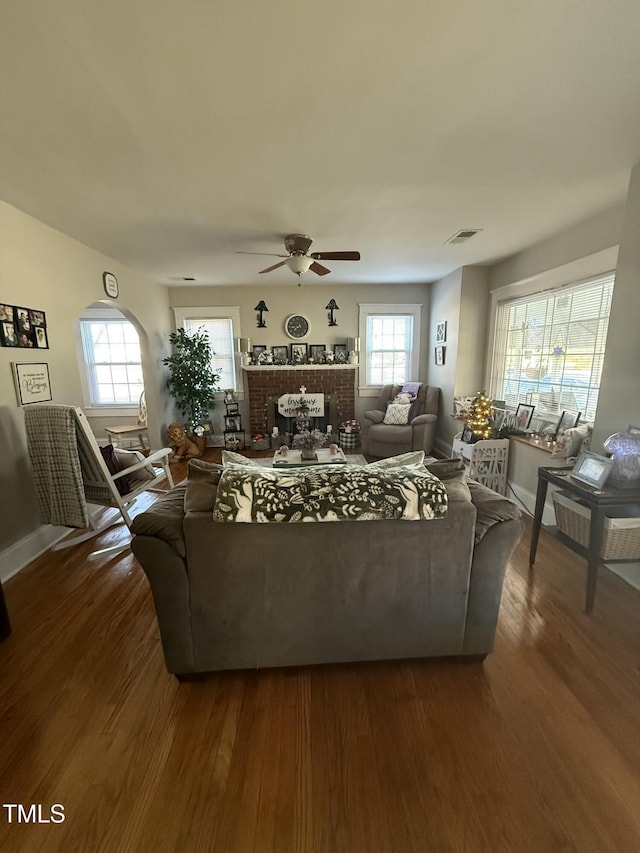 living area with visible vents, dark wood-type flooring, a ceiling fan, baseboards, and a brick fireplace