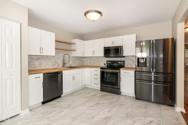 kitchen with appliances with stainless steel finishes, butcher block counters, a sink, light marble finish flooring, and white cabinetry