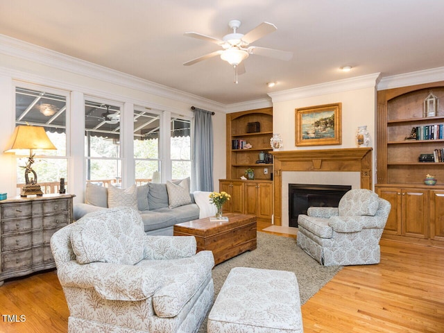 living area featuring light wood finished floors, a fireplace with flush hearth, ceiling fan, and ornamental molding