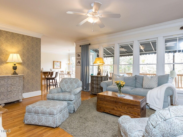 living room with a ceiling fan, wood finished floors, baseboards, wallpapered walls, and ornamental molding