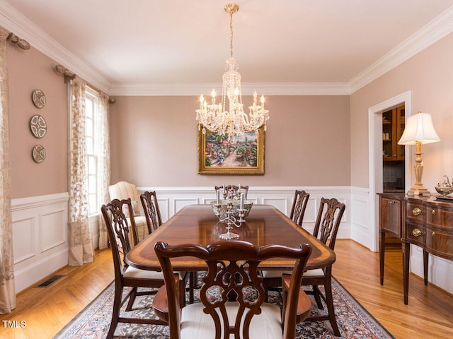 dining space featuring visible vents, light wood-style floors, a wainscoted wall, and crown molding