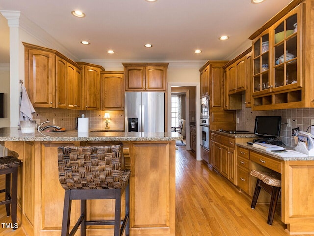 kitchen with light stone counters, a peninsula, stainless steel appliances, glass insert cabinets, and a kitchen bar