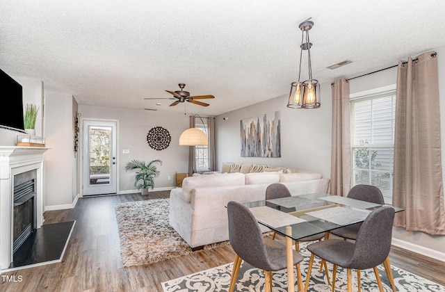 dining room featuring wood finished floors, a fireplace with raised hearth, visible vents, and a textured ceiling